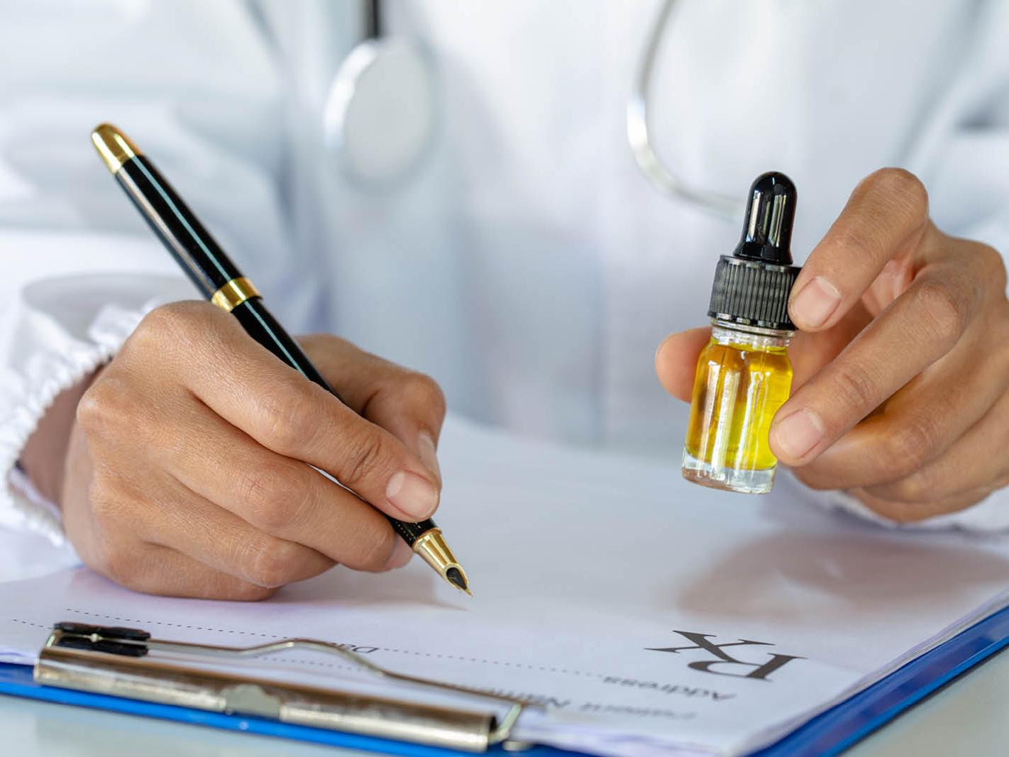 A person in a white doctor's coat writes on a clip board