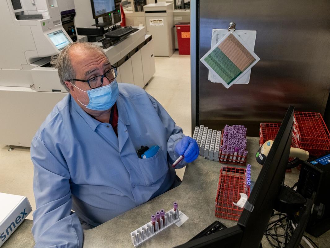 Daryl Weyandt wears a surgical mask and rubber gloves. In one hand is a vial. In front of him, other vials are propped on a plastic stand.