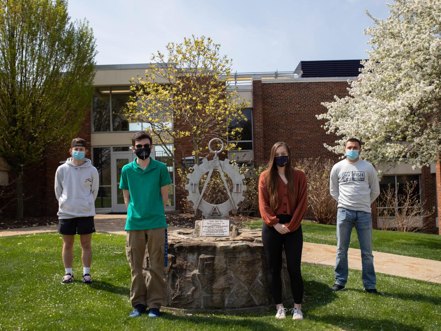 Four students stand outside by statue
