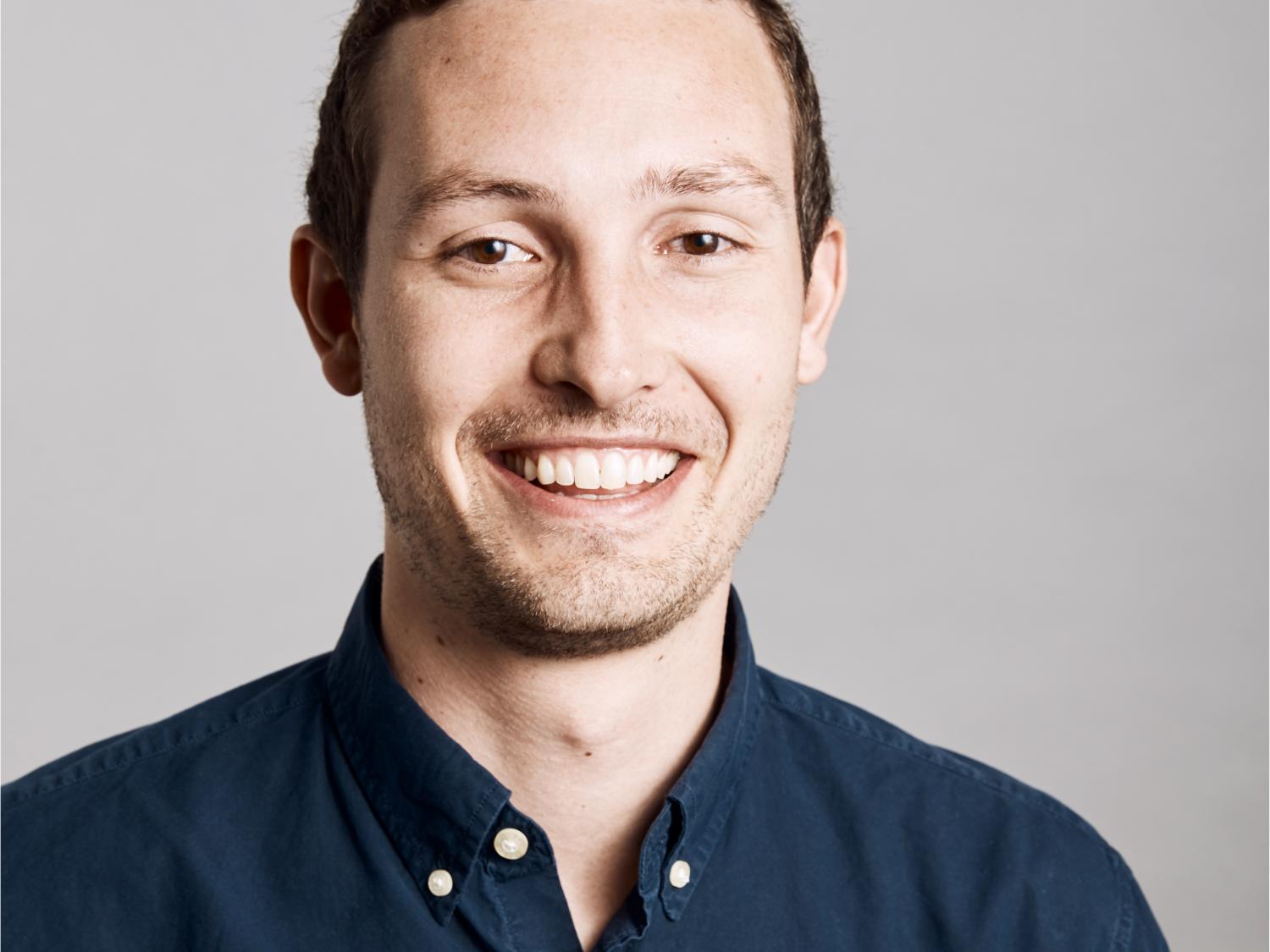 male in navy blue collared shirt smiles and poses for professional photo