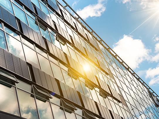 The sun shines on solar panels attached to a glass building.