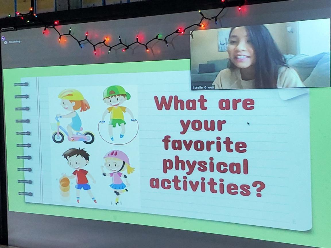 A computer screen shows Estelle Greene in a window in the upper left corner. The screen features the words “What are your favorite physical activities?” with animated characters.