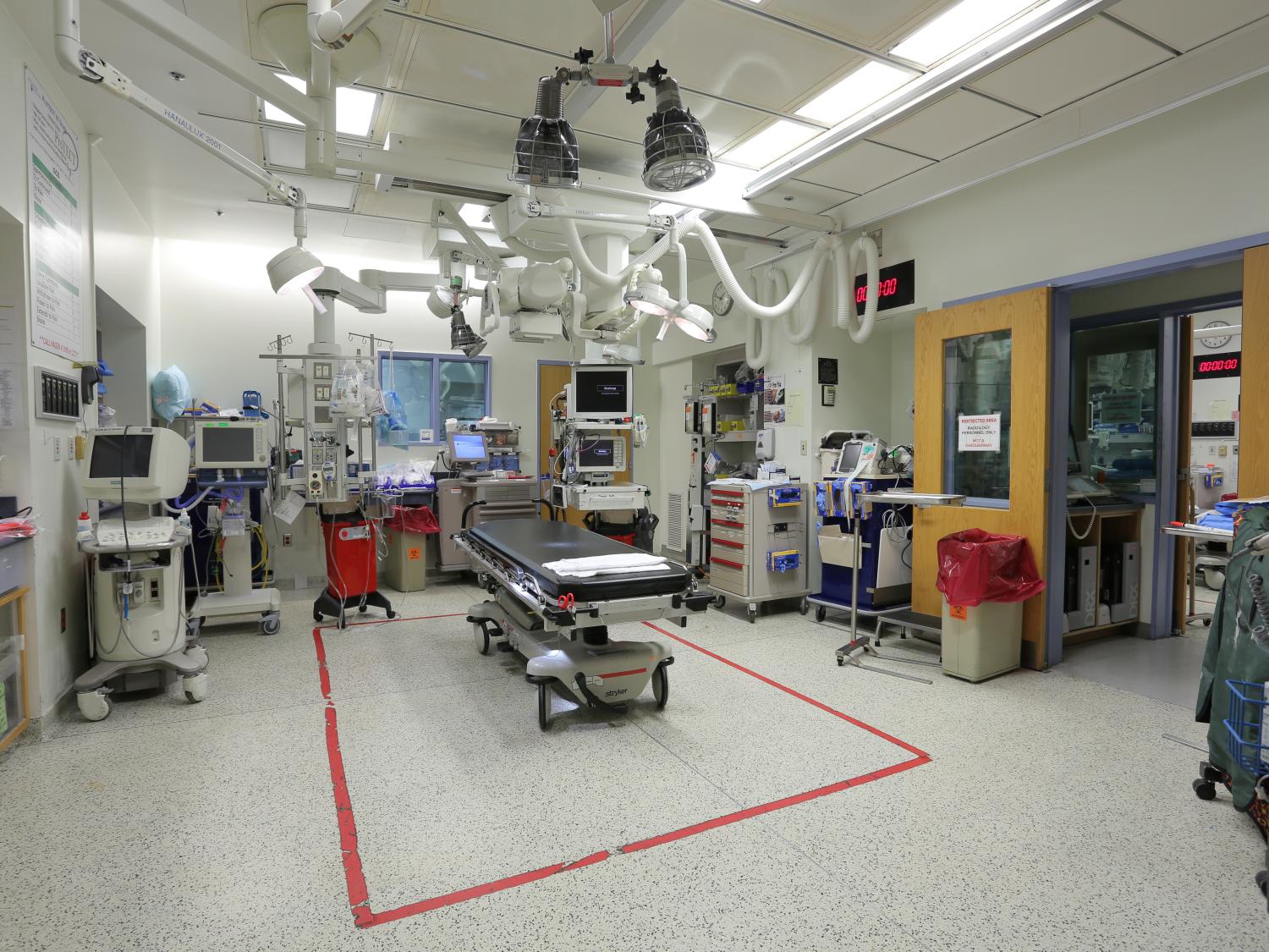 A wide shot of a trauma bay, which includes a treatment bed in the middle and medical equipment around the perimeter of the room and mounted to the ceiling.