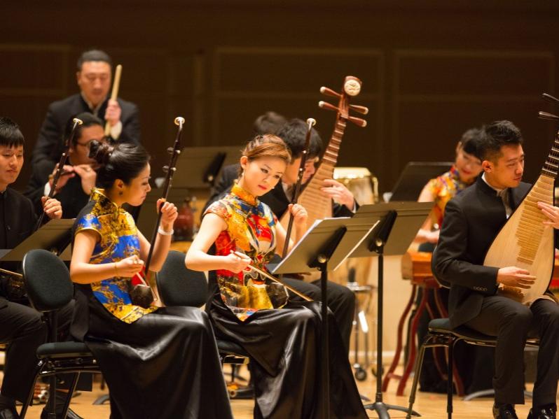 Musicians sit at music stands and play on traditional Chinese instruments.