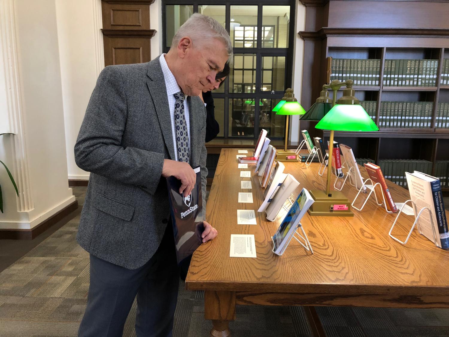 man standing looking down at large wooden table with books and written labels on display