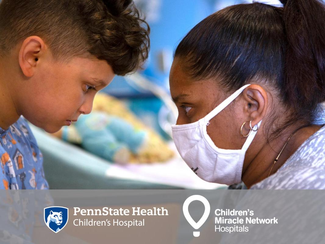 Side profile as a young child and an adult look each other in the eyes, each bearing a serious expression. A hospital bed is in the background, out of focus. At the bottom are logos for Penn State Children's Hospital and CMN.