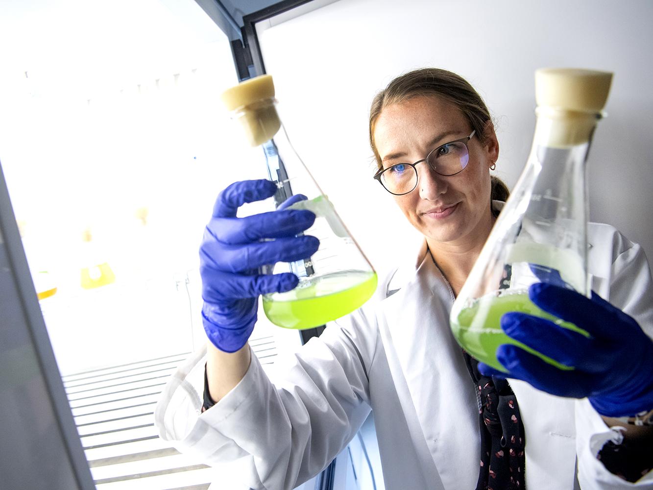 Sarah Princiotta, assistant professor of biology, holding up beakers in laboratory.