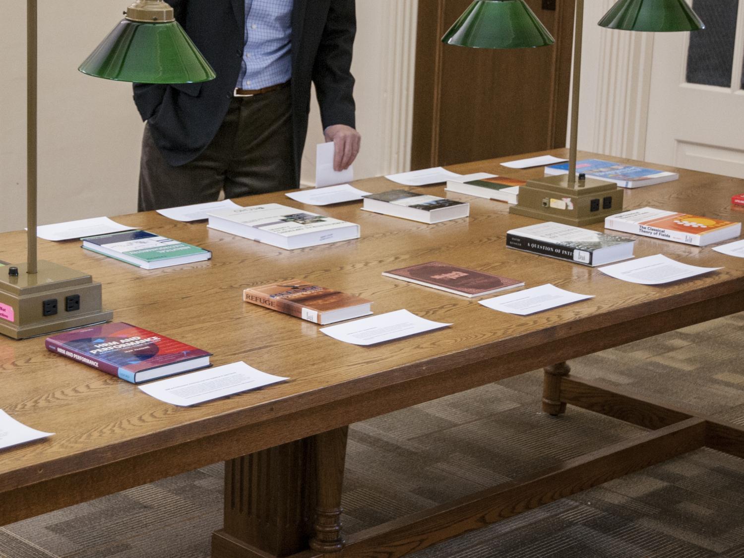 photo of wooden table holding books presented with papers describing why the books were selected, unidentified man looking at books on table
