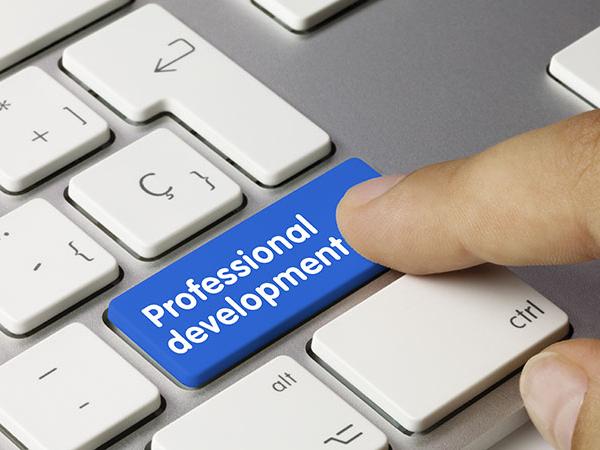 An index finger is about to push a button on a computer keyboard, but instead of a return key it is blue and says professional development.