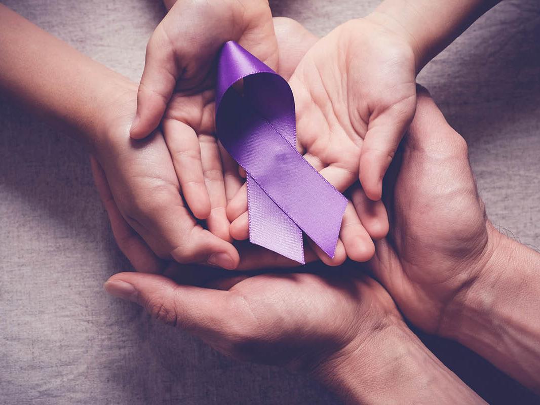 A close-up of three pairs of overlapping hands with a purple, curved ribbon placed on top.