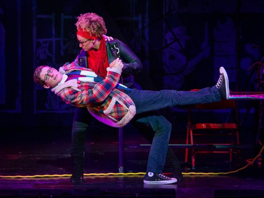 A woman holds a man in her arms as he kicks up one leg.