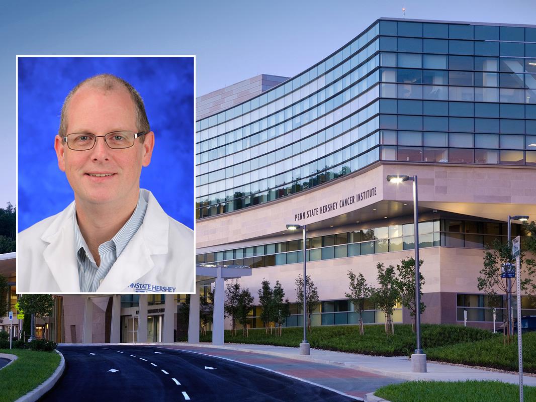 A head and shoulders professional photo of Douglas Stairs against a photo of Penn State Cancer Institute