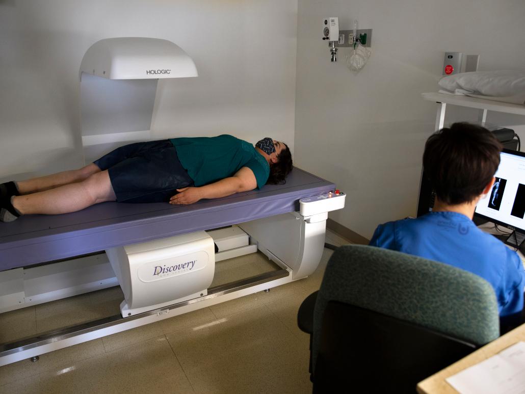 A woman lays on a table for an exam while a healthcare provider monitors her