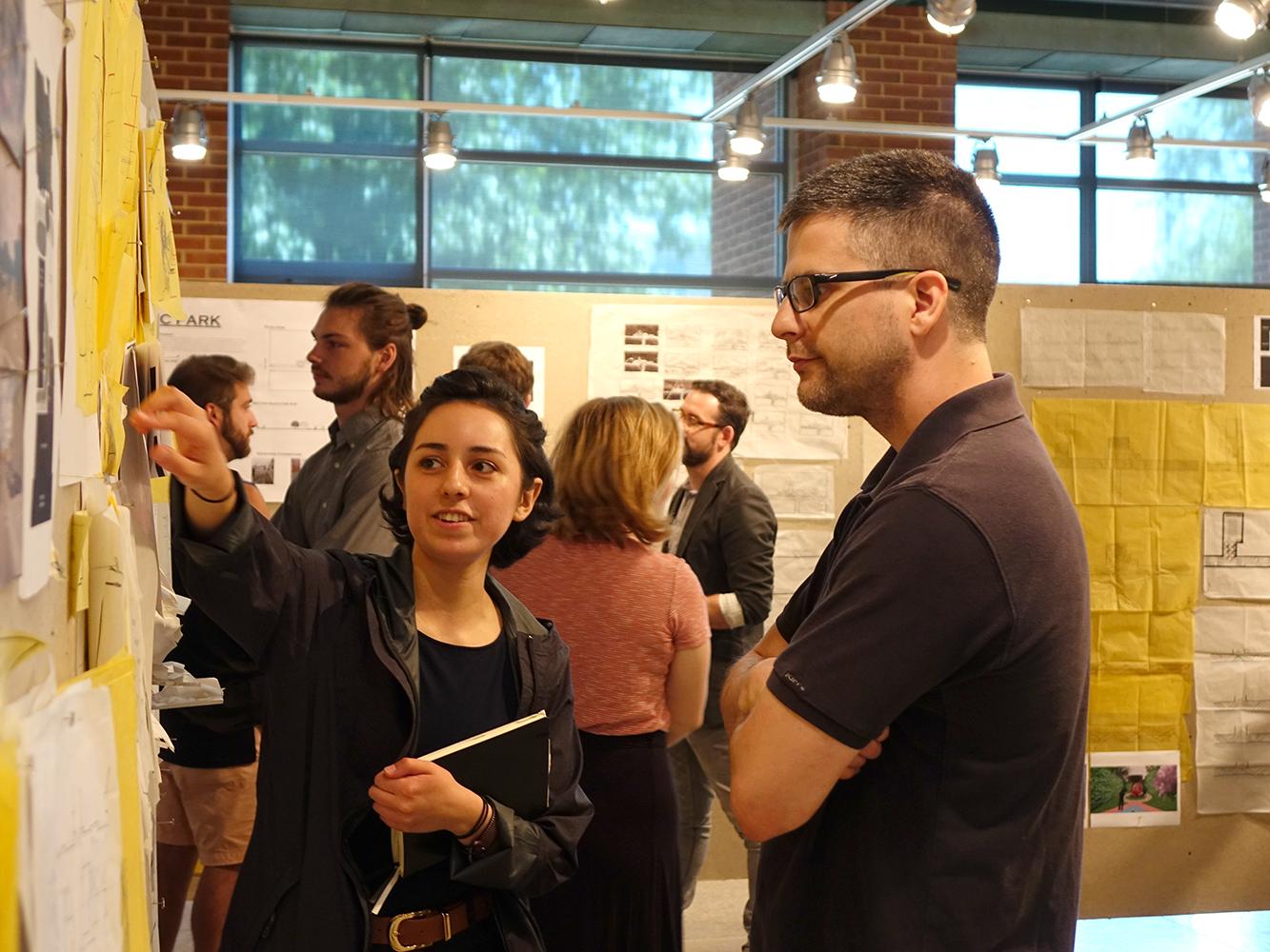 A female landscape architecture student points to her design during a critique by a landscape architecture faculty member.