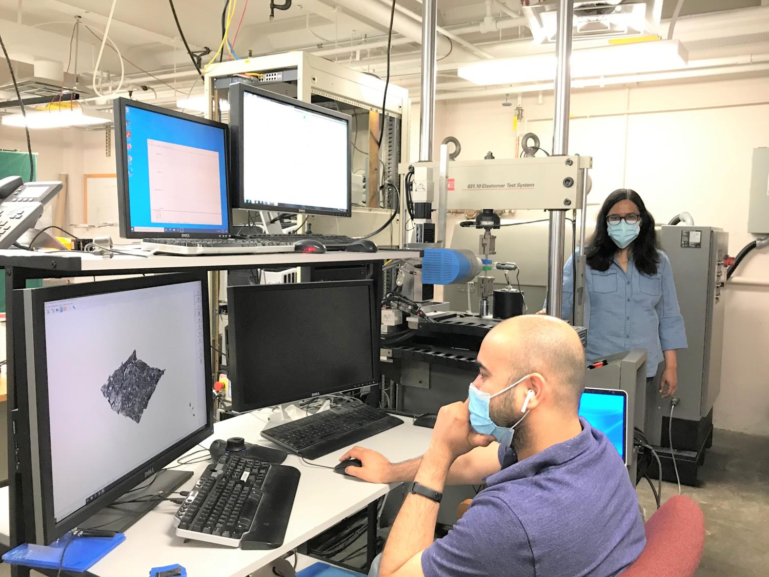 A graduate student and professor, both wearing masks and socially distanced, look at a computer monitor with data.