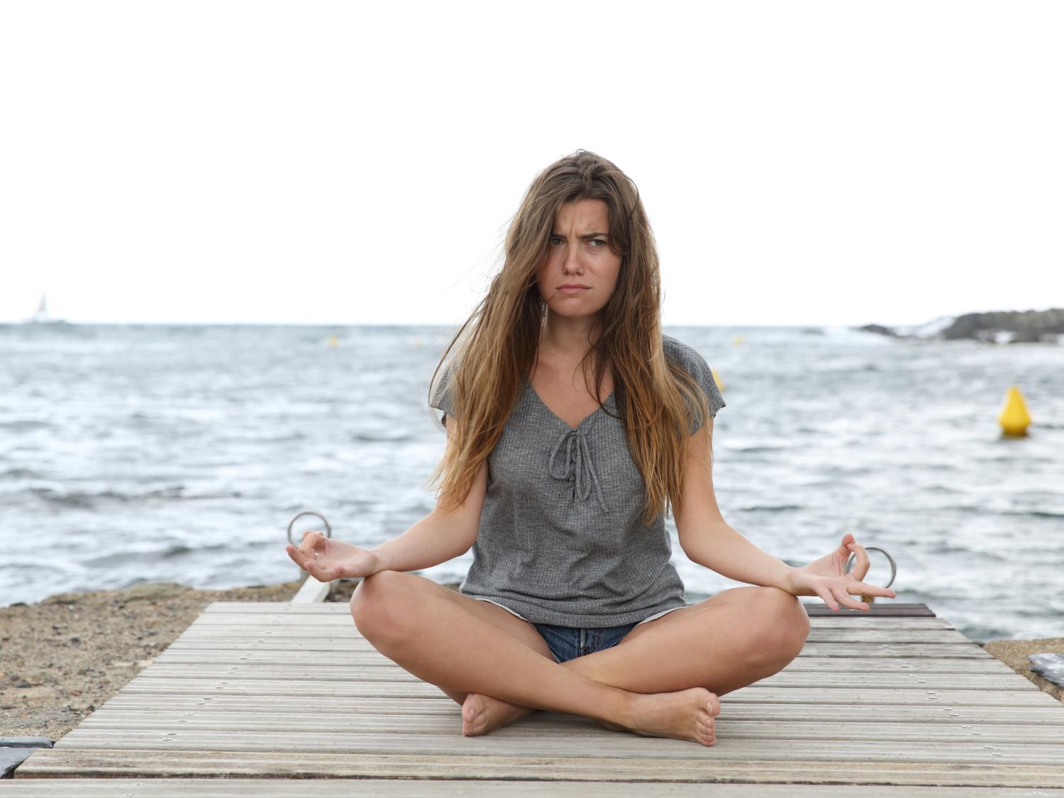 A woman sitting on a beach meditating with a worried expression