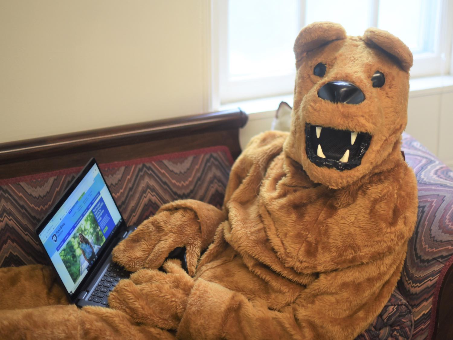 The Nittany Lion works on a laptop while reclining on a couch.