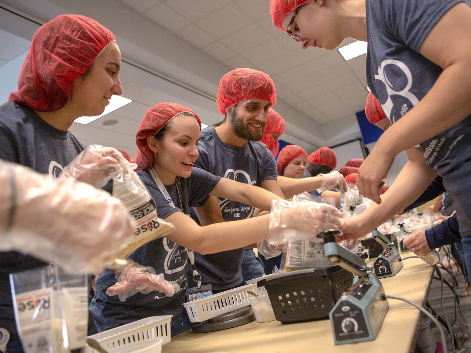 Four students stand around a table packaging bags of food.