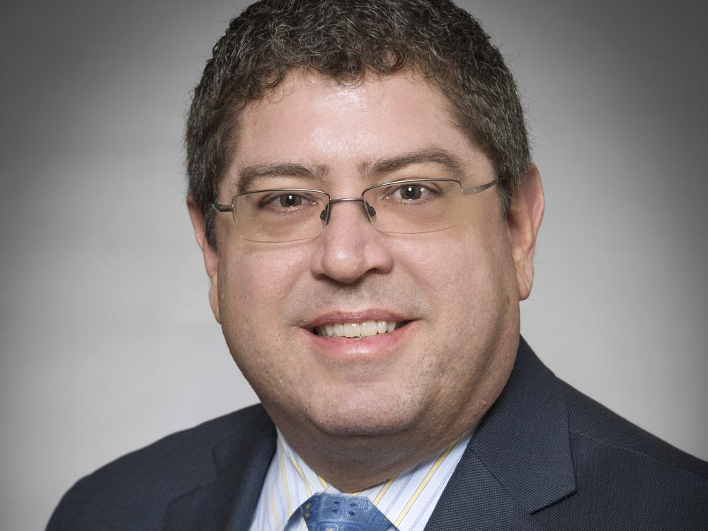 A man wearing a suit and glasses smiles for a photo