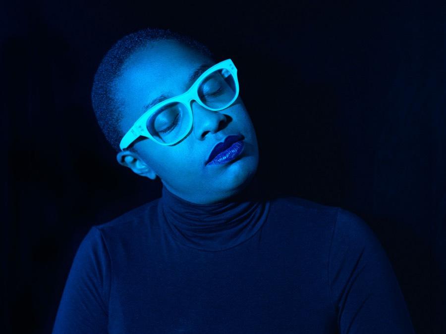 The singer, wearing thick-rimmed glasses, cocks her head to her right.