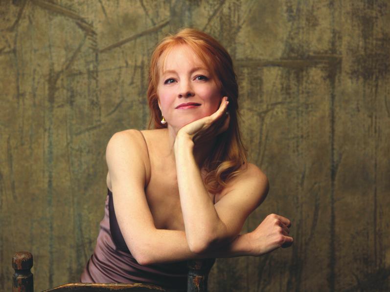 Jazz composer Maria Schneider sits in a wooden chair with her arms crossed on one of the posts.