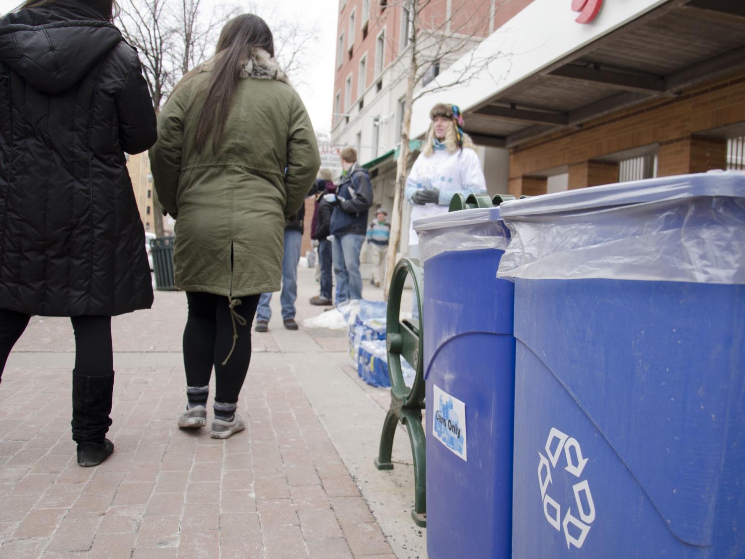 Recycling bins downtown with students handing out water in the background