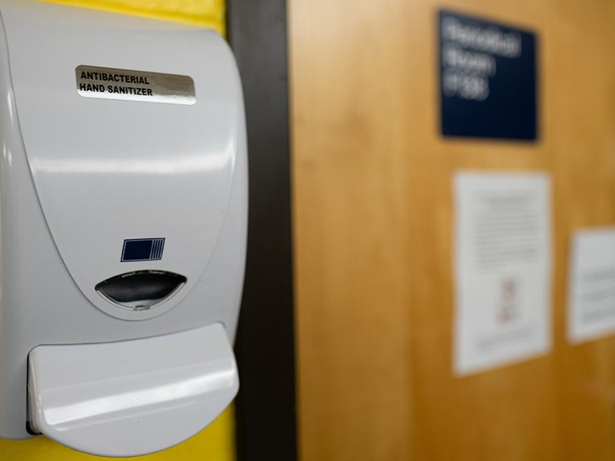 A hand sanitizer pump hangs on a wall next to a door. 