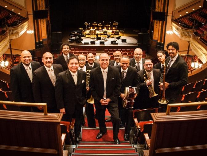 A group of musicians smile while standing on the balcony level of an auditorium.