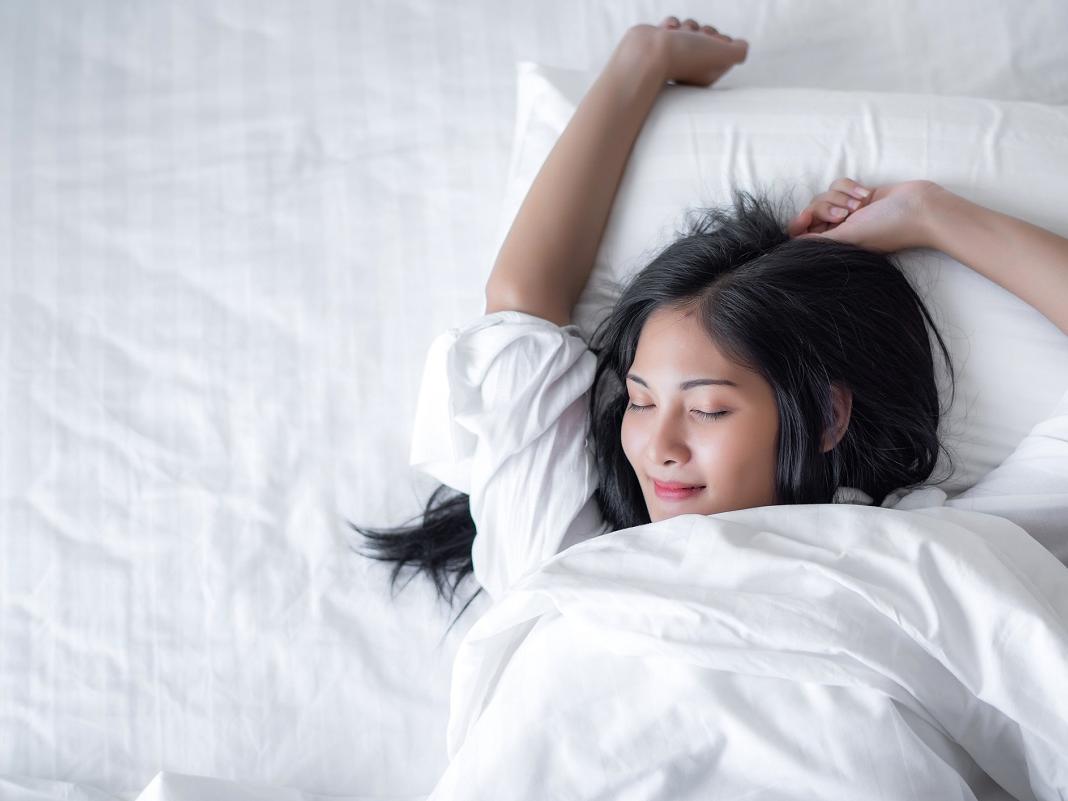 Young woman wakes up happy with a smile on her face in bed in the morning.