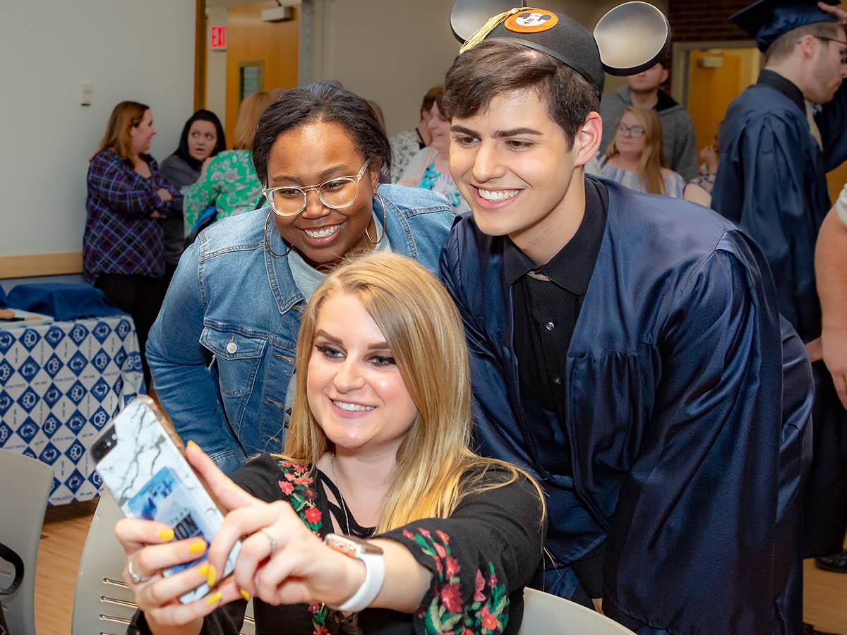 A graduate poses with two friends for a selfie.