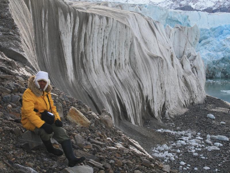 Multimedia artist Paul D. Miller, aka DJ Spooky, sits on rocks positioned near icicles in the Arctic region.