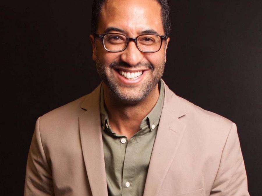 A man wearing glasses and shown from the shoulders up smiles.