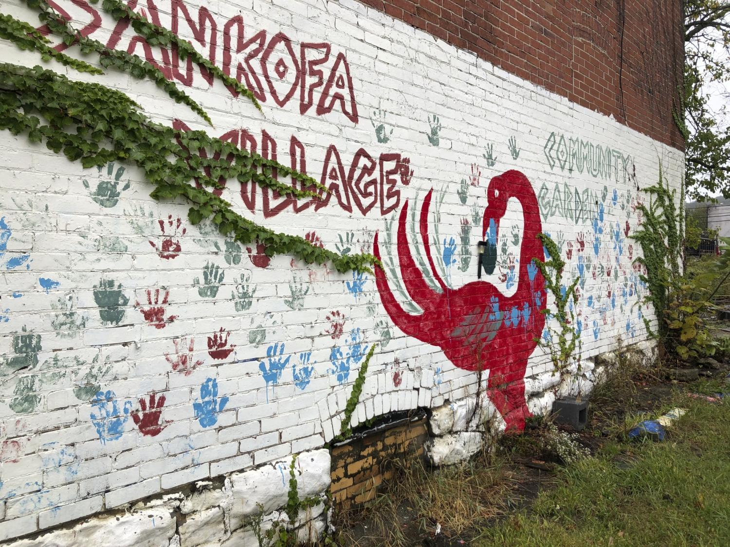 A brick wall that is painted white with a flamingo painted on it as well as Sankofa Village and the handprints of children in blue and red.