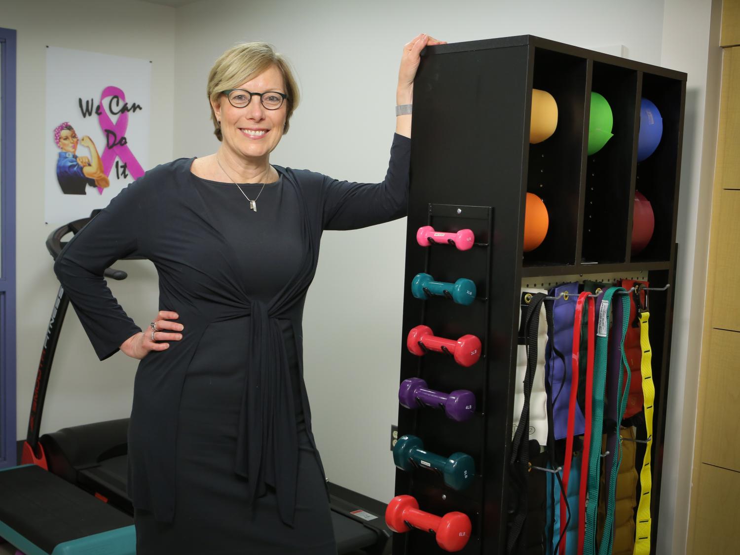 Kathryn Schmitz poses for a photo, leaning against a rack that contains exercise equipment.