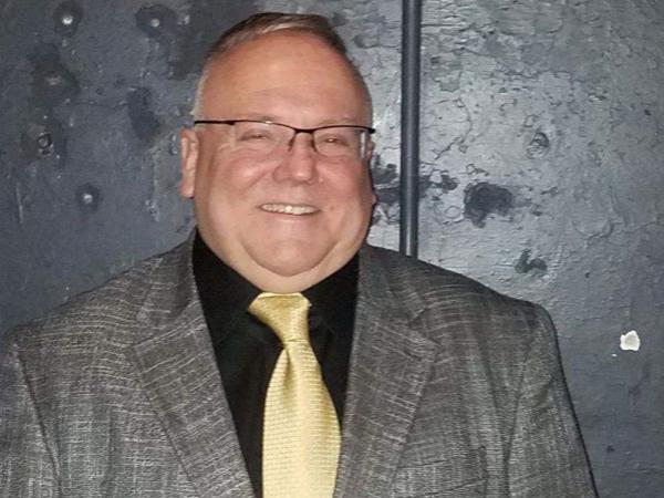 A photo of Scott Noxon wearing a grey jacket and yellow tie.