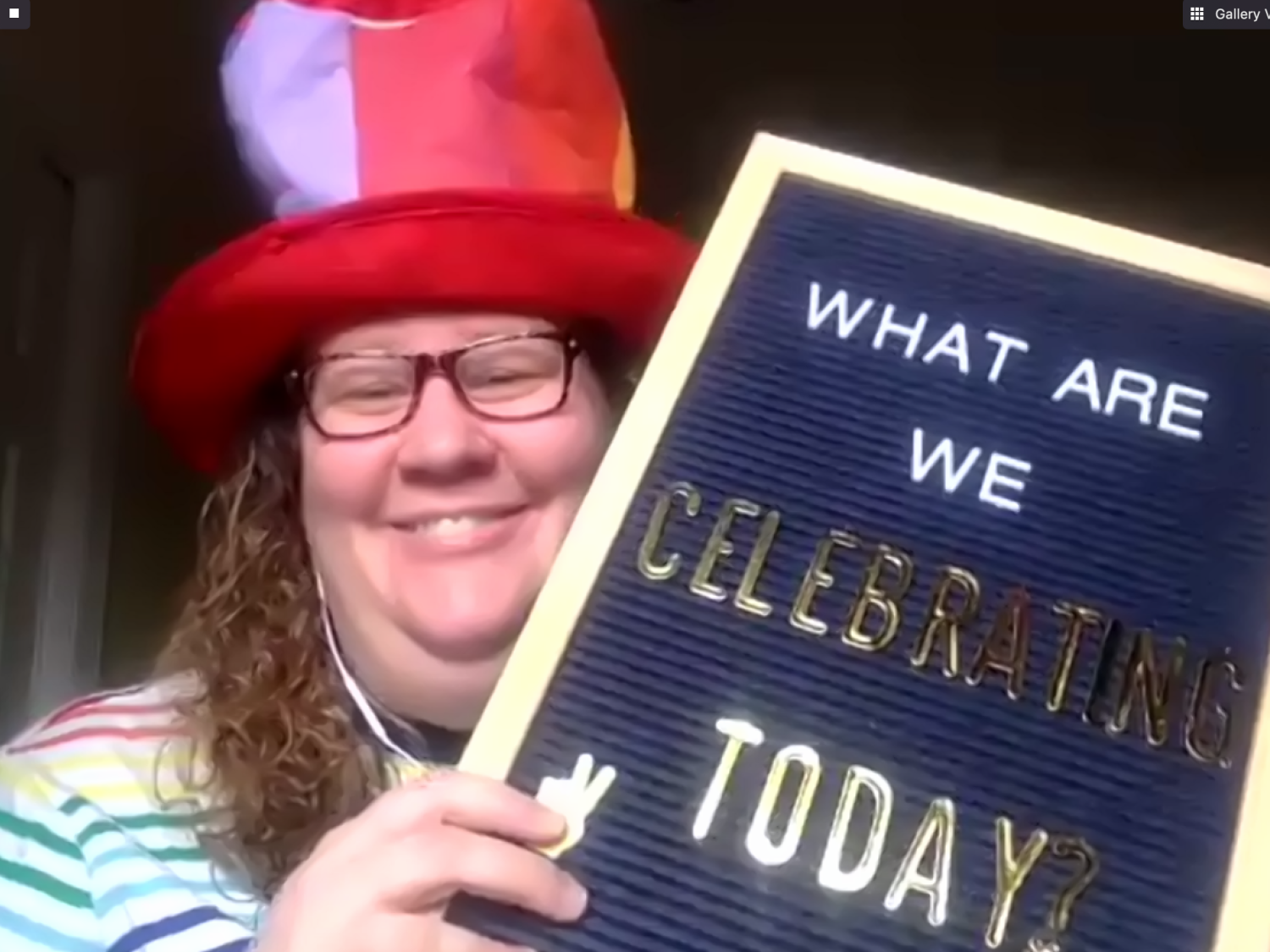 A woman smiles with a rainbow-striped hat and holds up a letter board saying, "what are we celebrating today?"