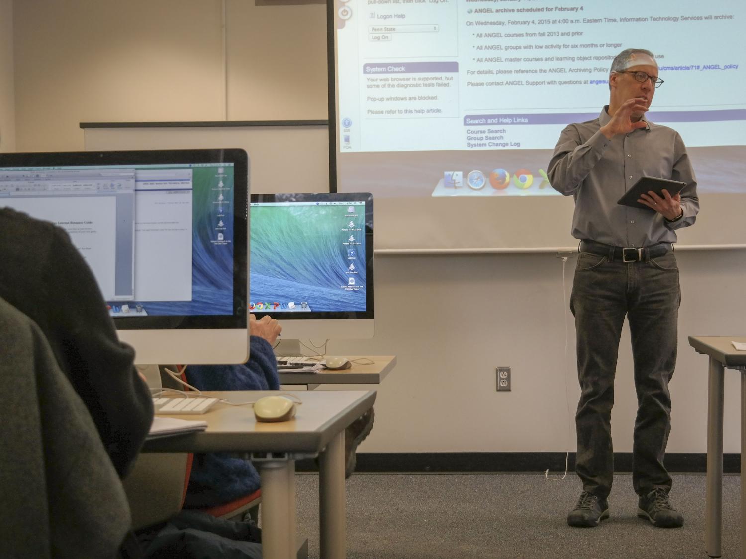 An instructor uses an iPad at the head of a classroom