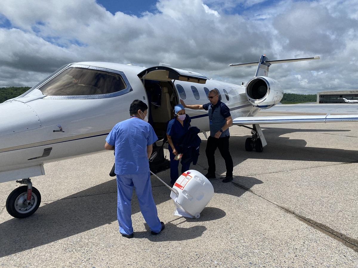 Two people unload a donor transport device from a plane