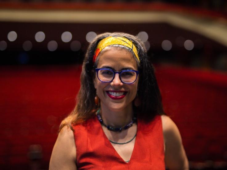 A woman wearing glasses and a headscarf smiles.