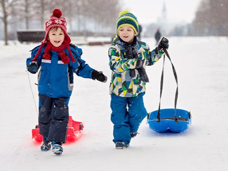 Two children pulling sleds in the snow.