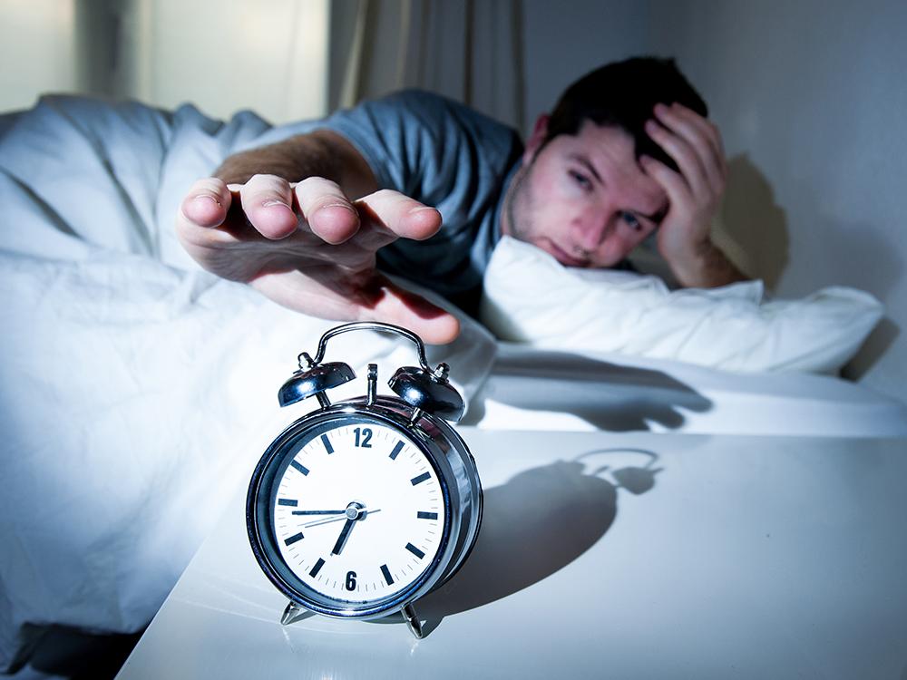 Man in bed reaches over to hit alarm clock.