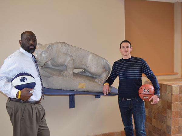 Two Penn State staff members standing with basketballs next to the Nittany Lion located in the campus' atrium area