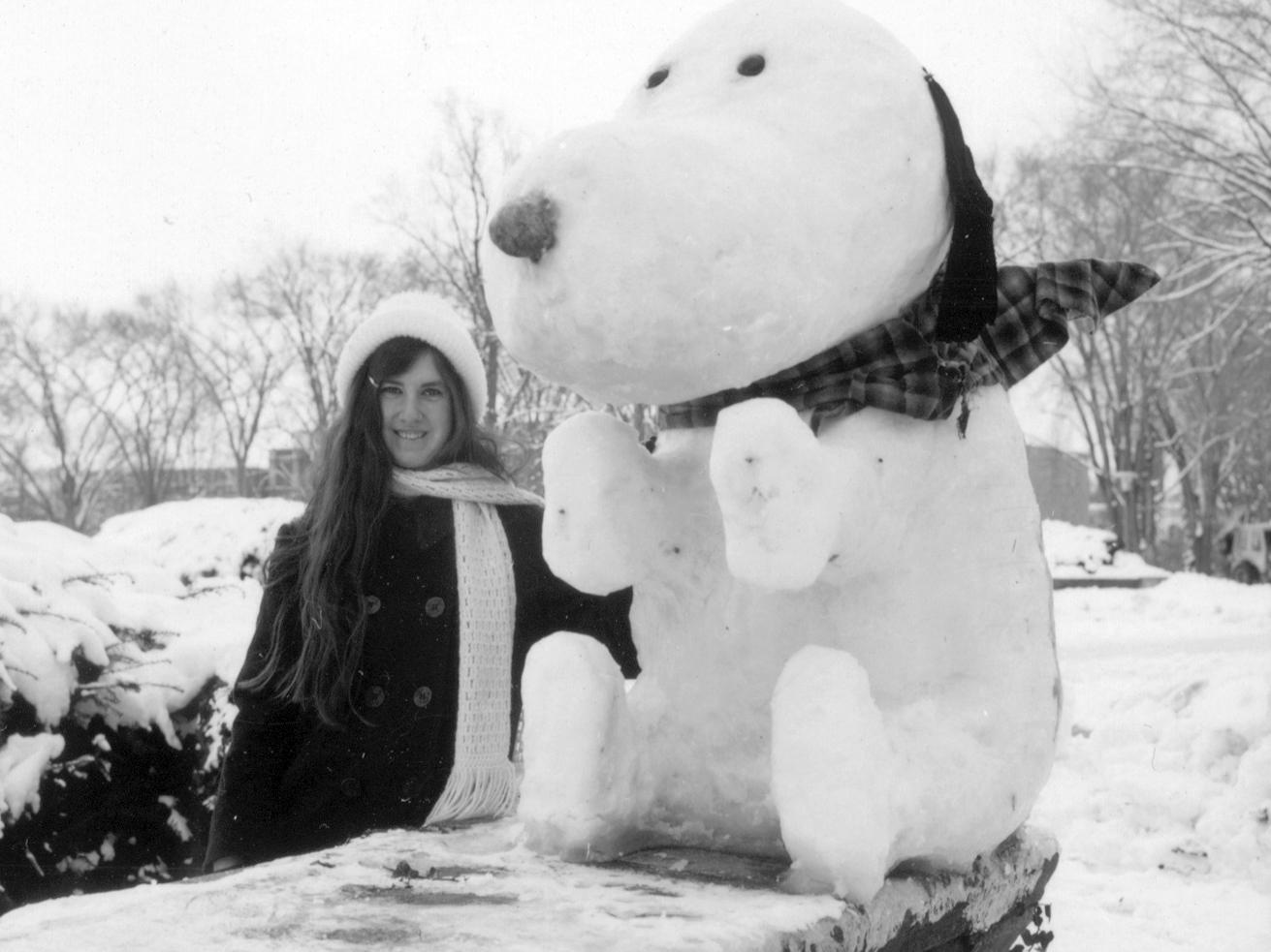 A student in 1975 standing next to a Snoopy made of snow on Old Main steps