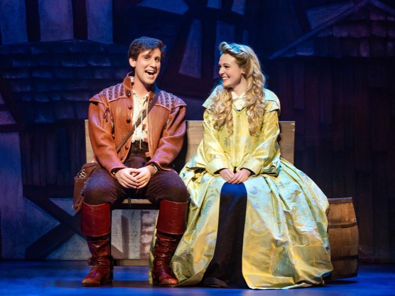 A man and woman dressed in medieval costumes sit on a box and smile at each other.