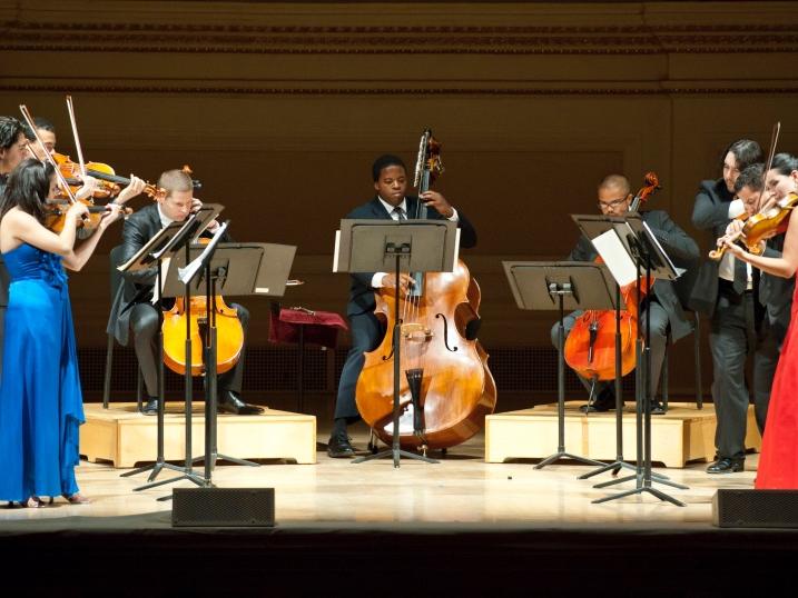 A group of formally dressed musicians perform on a stage.