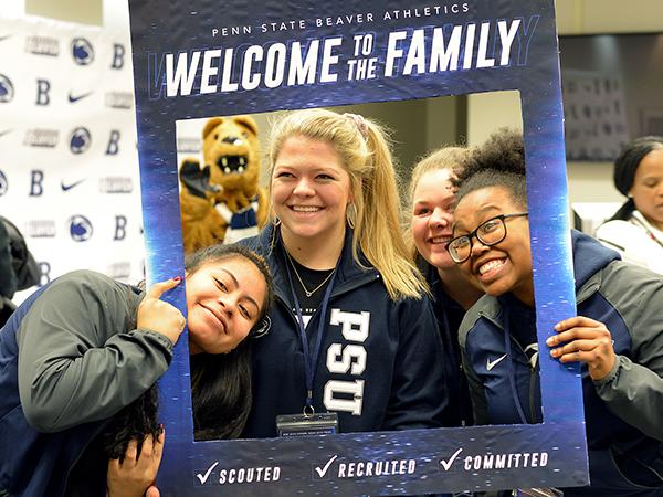 Three female students pose for a photo while holding a Penn State Welcome picture frame around themselves.