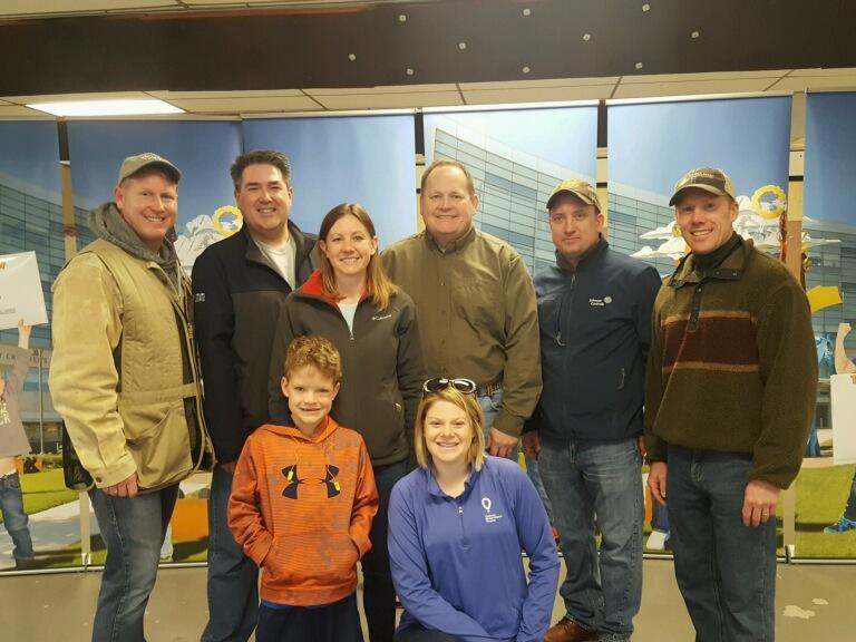 Eight people -- seven adults and one child -- pose for a photo in front of a multi-part backdrop depicting Penn State Children's Hospital.