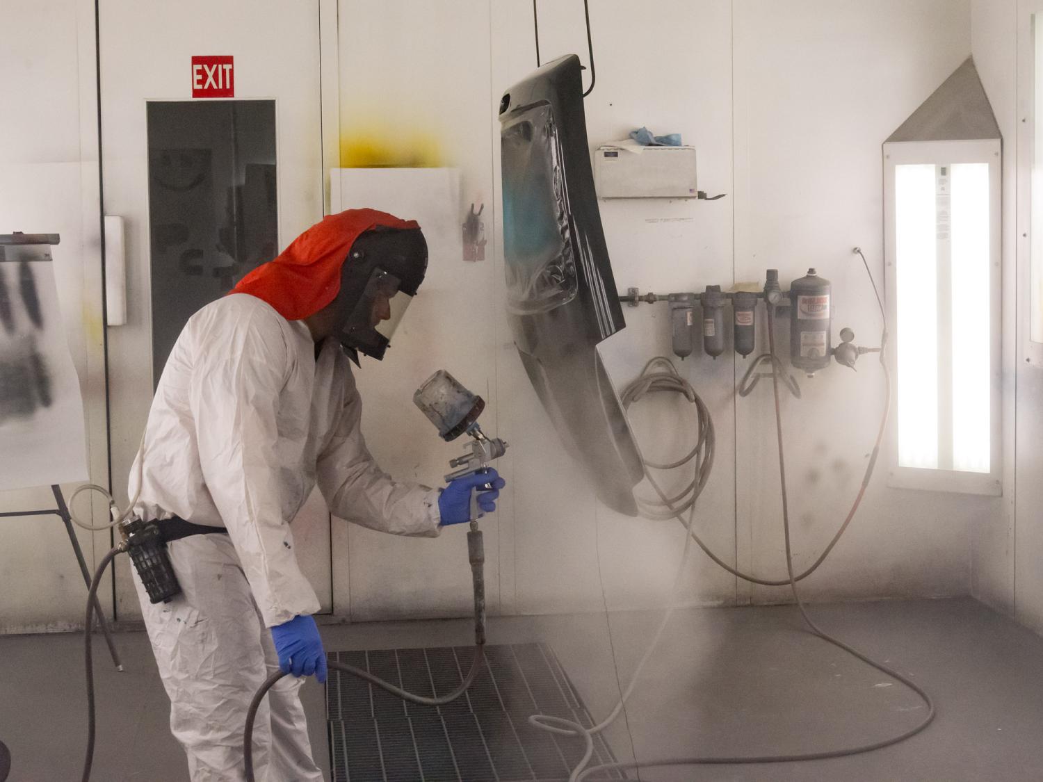 A person wearing protective gear sprays paint in a paint booth.