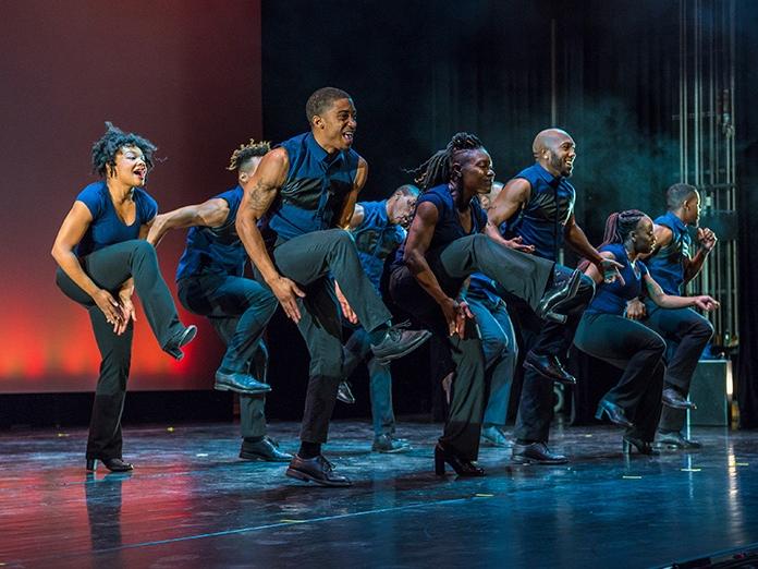 A group of dancers bring their knees up high while dancing on a stage.
