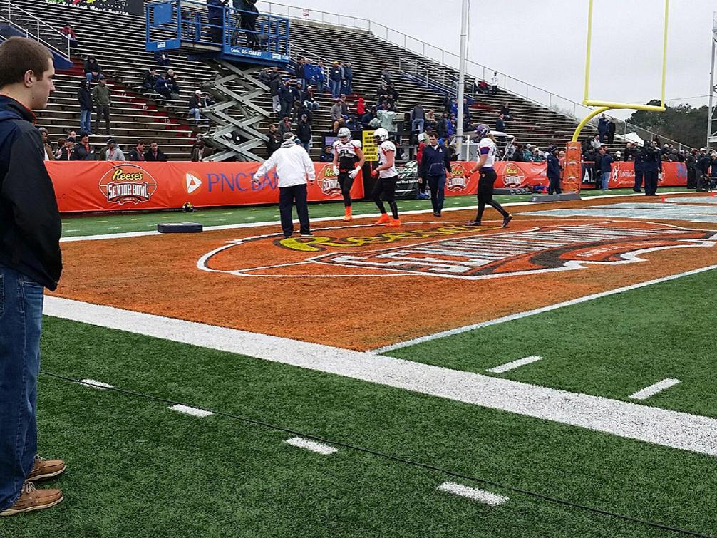 Penn State senior Ryan Stevens (foreground, left) watches a Senior Bowl practice as part of his duties as a media relations volunteer at the game.